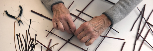 Hände arbeiten mit Zweigen an Wandarbeit aus Draht und Naturmaterial